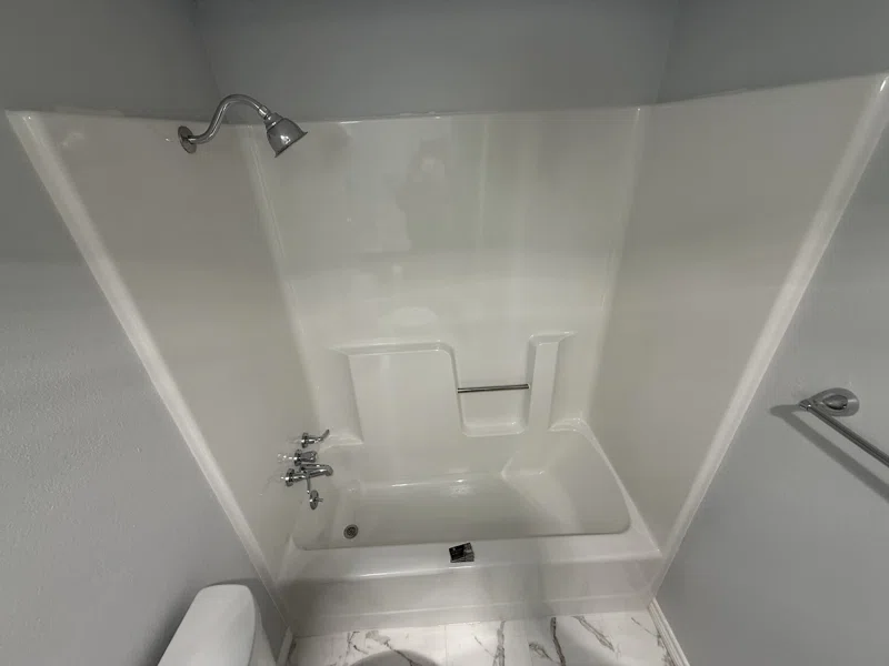White one-piece tub and shower surround with molded shelves.