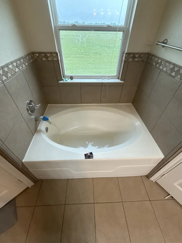 Oval soaking tub below a window with a tiled surround.