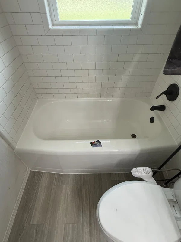 Light-colored bathtub with black fixtures and white subway tile.