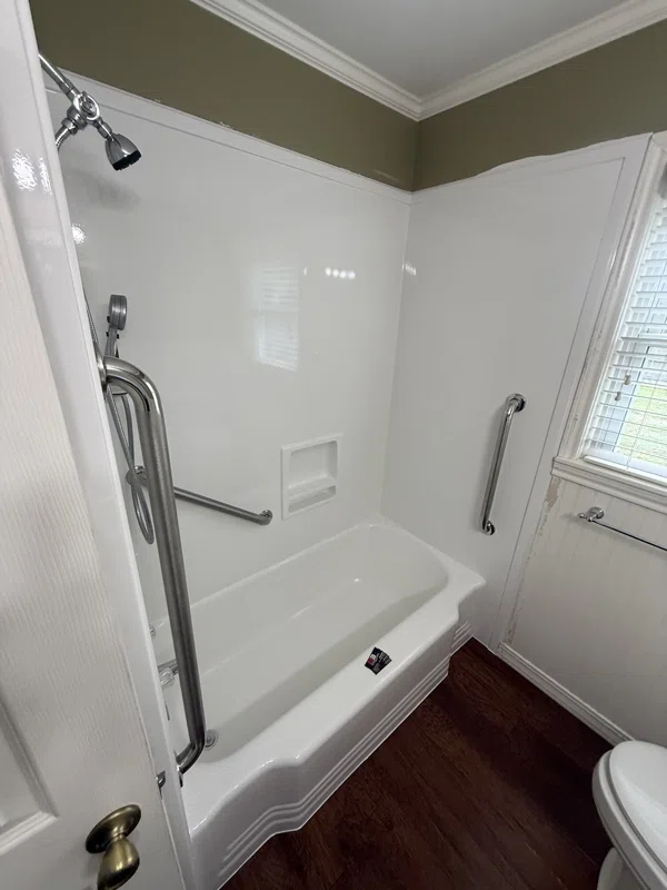 White tub and shower surround with molded shelves and grab bars.