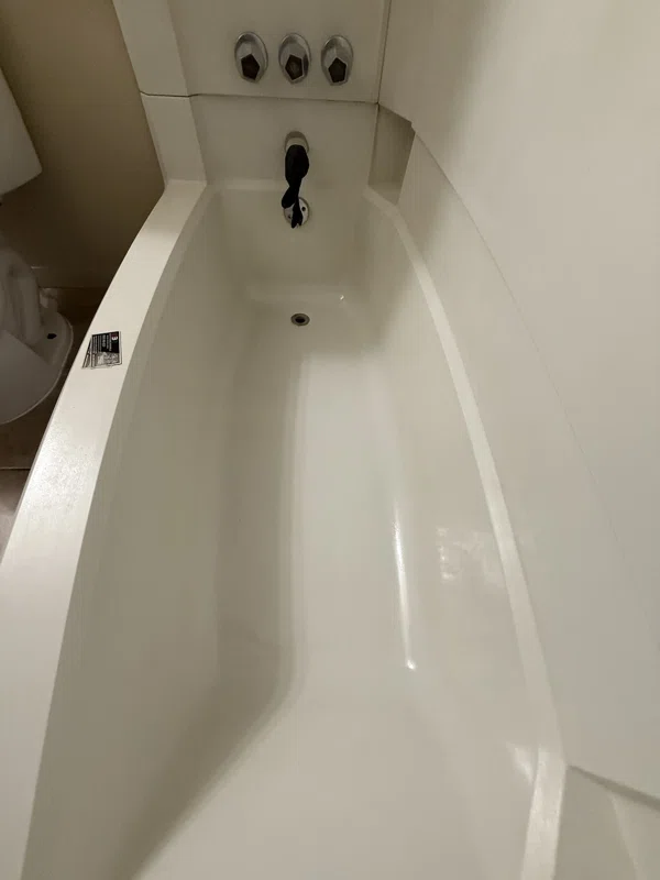 White bathtub viewed along its length beside a light-colored wall surround.