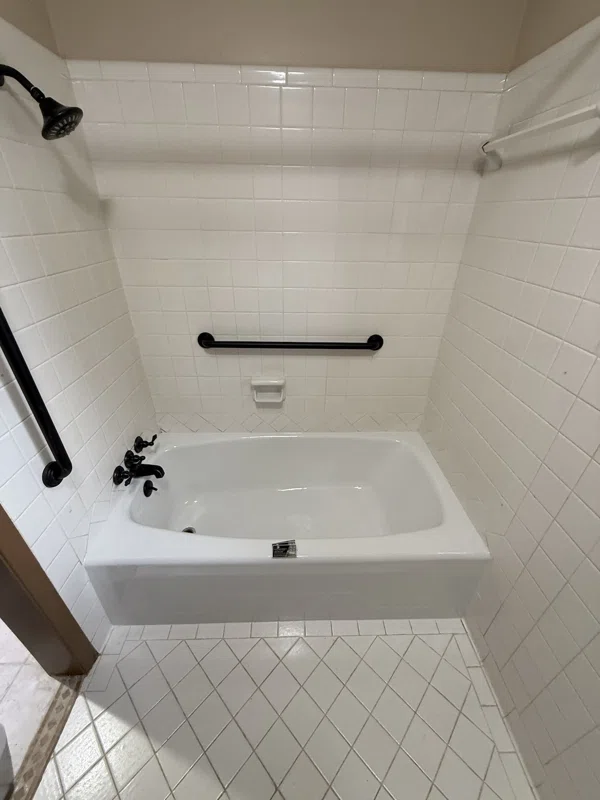 White bathtub and white tile surround with black fixtures and a grab bar.