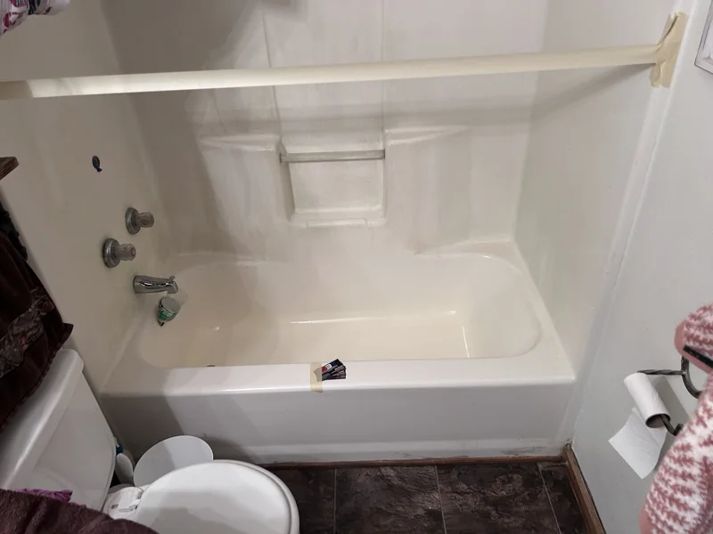 Light-colored bathtub and surround with a molded soap dish.