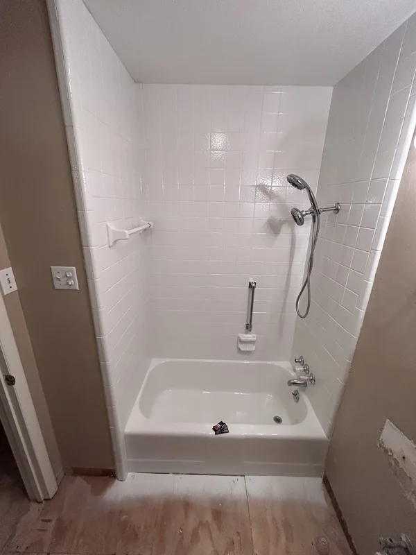 Compact white bathtub with a tiled surround and a handheld shower.