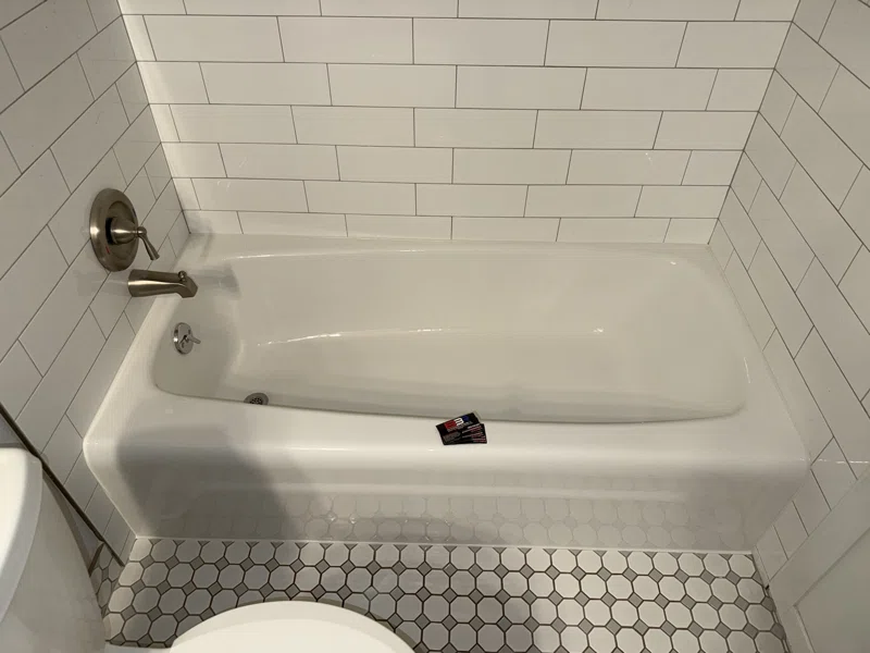 White bathtub beside white subway tile and a small hexagonal tile floor.
