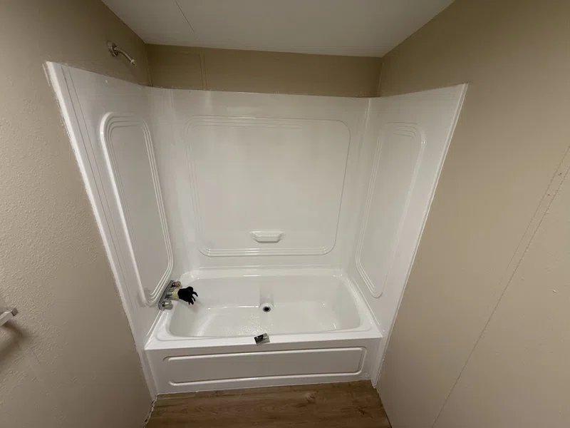 White bathtub and molded shower surround with shelves.