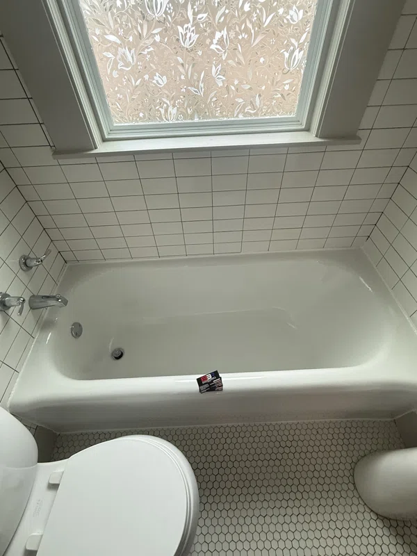 White bathtub below a window with a tiled surround.