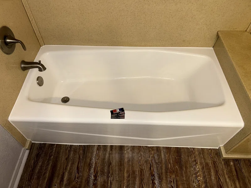 White bathtub with a molded front apron, dark fixtures and tan wall surround.