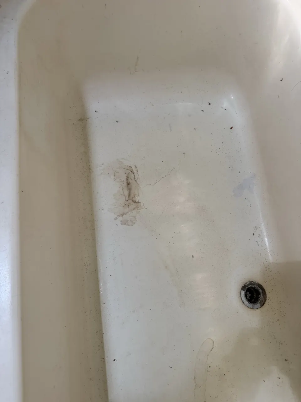 Worn bathtub floor with visible cracks and surface damage
