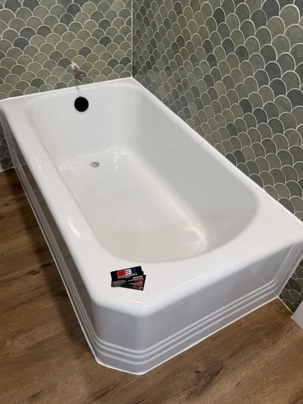 White bathtub with a molded front apron beside green scalloped tile.